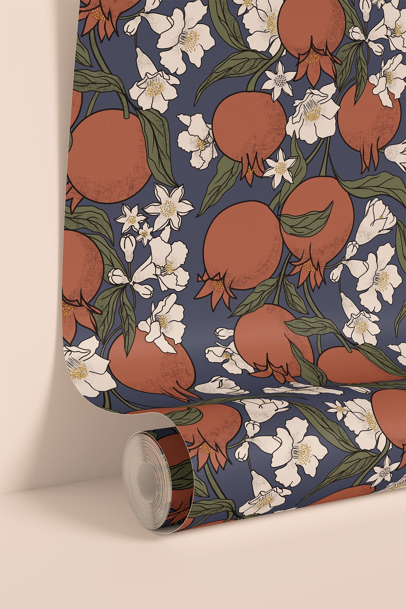 A roll of wallpaper with a repeating pattern of pomegranates, white flowers, and green leaves on a dark blue background, shown partially unrolled against a warm beige wall.