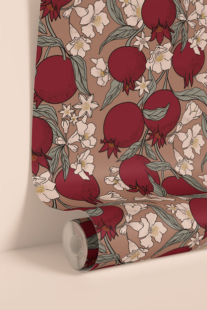 A roll of wallpaper or fabric with a repeating pomegranate and white floral pattern on a warm taupe background, shown partially unrolled against a clean cream wall.