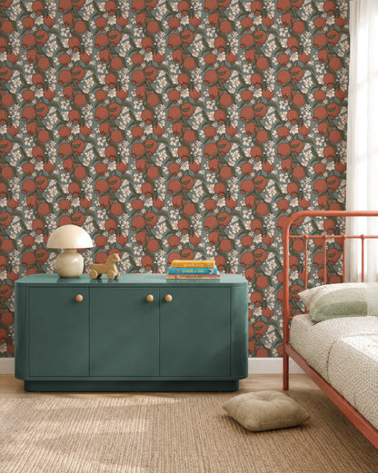 A styled bedroom corner featuring a dark green wallpaper with a repeating pattern of red-orange pumpkins and white flowers. A teal green sideboard cabinet with gold knobs sits against the wall, styled with a mushroom lamp and books, next to a rust-orange metal bed frame.