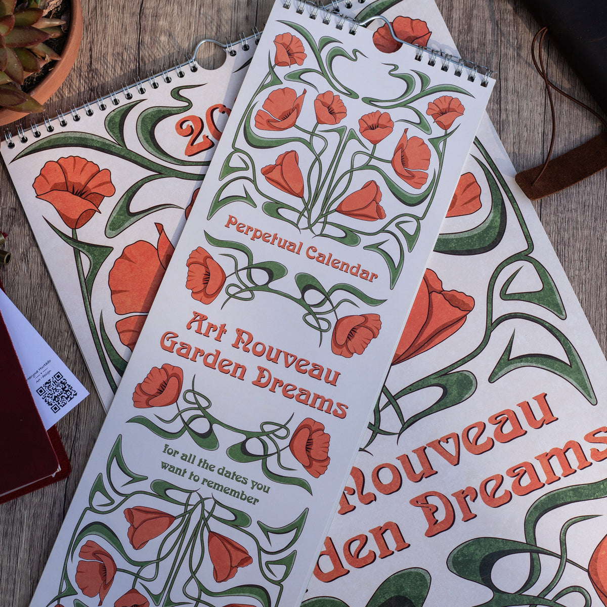 Two Art Nouveau Garden Dreams calendars with poppy covers overlapping on a wooden table