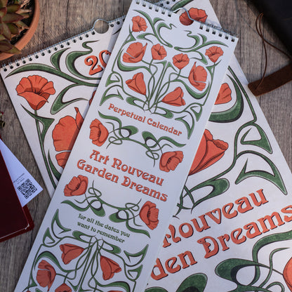 Two Art Nouveau Garden Dreams calendars with poppy covers overlapping on a wooden table