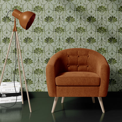 A mid-century modern accent chair upholstered in rust-brown velvet with light wood legs, set against a green and white Art Deco patterned wallpaper. A matching rust-brown tripod floor lamp stands to the left on a stack of books.