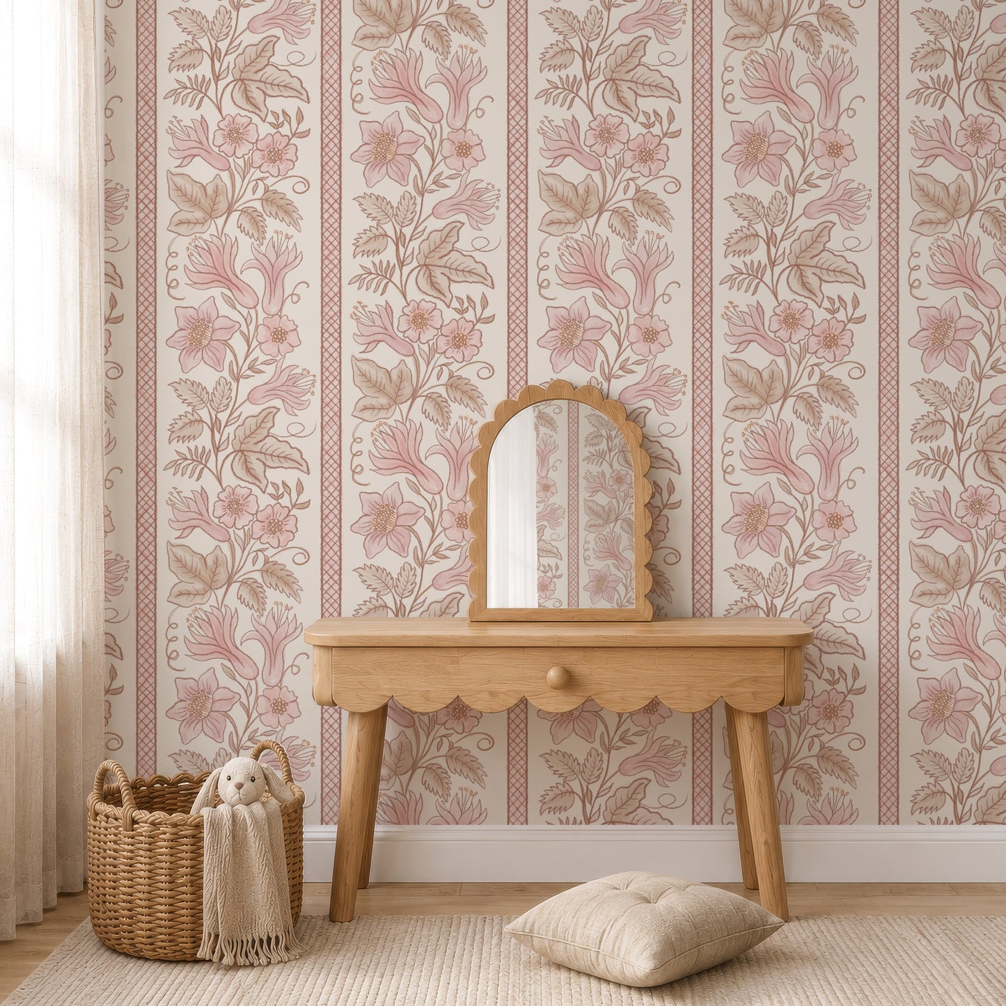 A styled interior scene showing floral wallpaper with vertical pink and beige botanical stripes, a light wood console table, a matching arched mirror, a woven basket with a cream throw and plush toy, and a beige cushion on a rug.