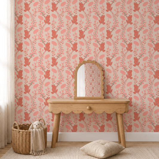 A styled interior scene showing a wall covered in pink and coral frogs wallpaper, with a light wood console table, small arched mirror, woven basket, throw blanket, and a cushion on a cream rug