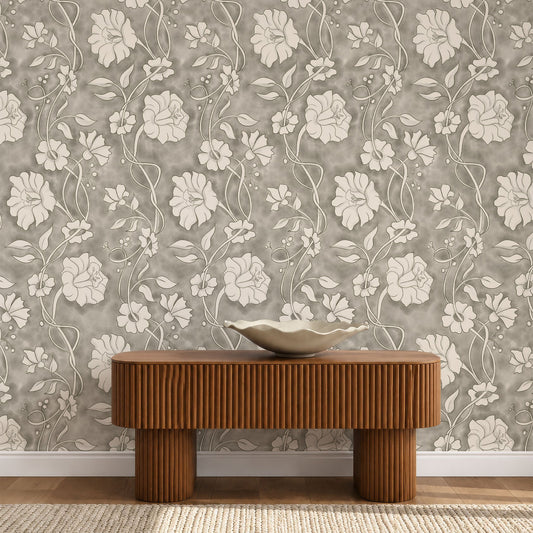 A styled interior scene showing a floral wallpaper with a repeating cream and taupe botanical pattern on a warm gray background, behind a low ribbed wooden console table with a ceramic bowl on top.