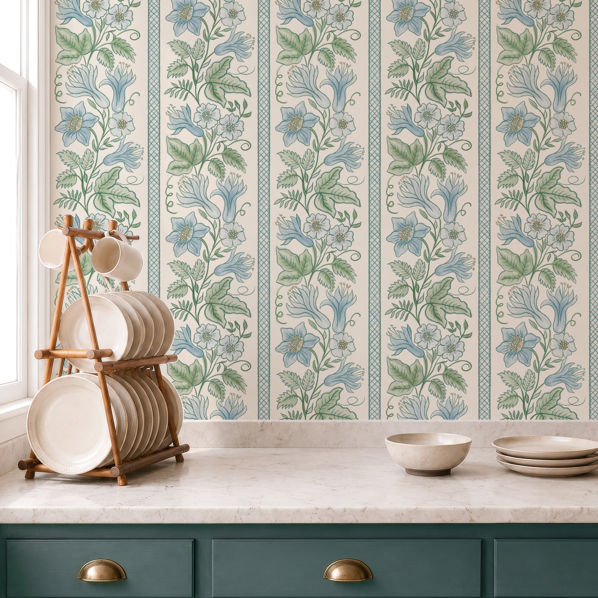 Floral wallpaper with vertical stripes of blue flowers and green leaves on a cream background, shown in a kitchen setting behind a marble countertop with a wooden plate rack and teal cabinets.