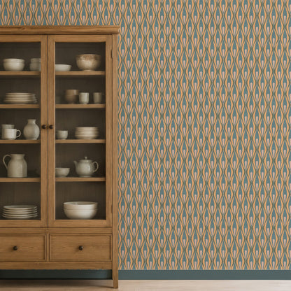 A wooden display cabinet stands against a wall covered in 70s style wallpaper with beige, blue, and brown ogee motifs. The cabinet has glass upper doors and two lower drawers, with white dishes and ceramic vessels on the shelves.
