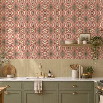 A styled kitchen interior featuring pink patterned wallpaper with a repeating geometric motif, sage green cabinets, a white countertop, and warm natural light from a window.