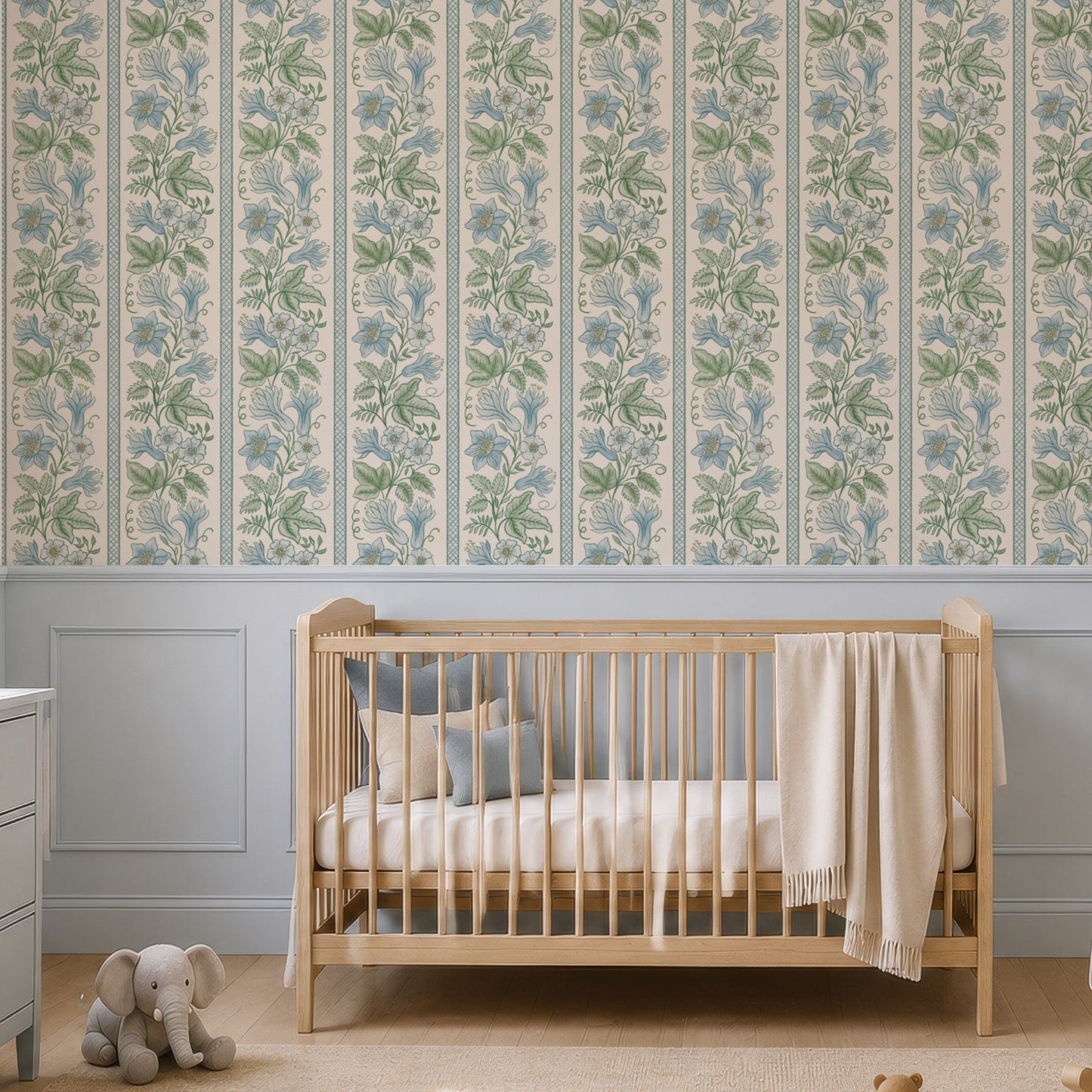 A styled nursery room featuring a wall covered in vertical floral wallpaper with a light blue and green botanical pattern. The room is furnished with a light wood crib, a pale blue rocking chair, a matching blue-gray dresser, and a beige rug with wooden toys.