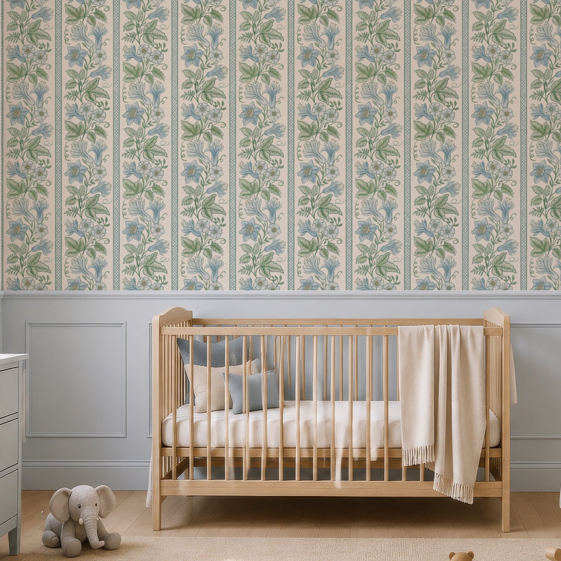 A styled nursery room featuring a wall covered in vertical floral wallpaper with a light blue and green botanical pattern. The room is furnished with a light wood crib, a pale blue rocking chair, a matching blue-gray dresser, and a beige rug with wooden toys.