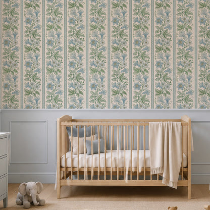 A styled nursery room featuring a wall covered in vertical floral wallpaper with a light blue and green botanical pattern. The room is furnished with a light wood crib, a pale blue rocking chair, a matching blue-gray dresser, and a beige rug with wooden toys.