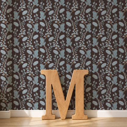 Dark brown wallpaper with a repeating light blue and beige frogs pattern, shown in a room setting with a light wood floor and a large wooden letter 'M' in the foreground.