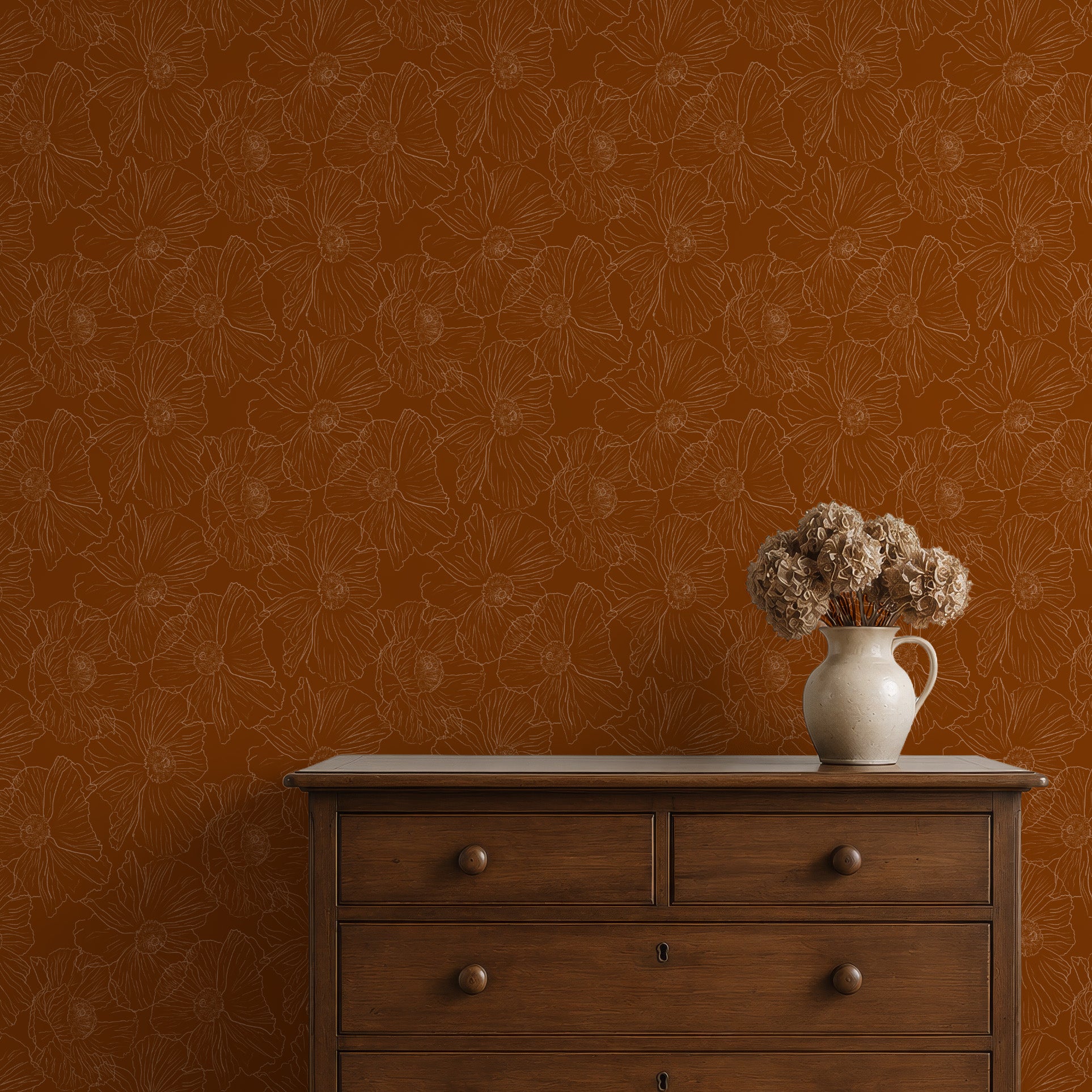 A styled interior scene showing a warm rust-orange wallpaper with a subtle floral line pattern, a dark wood dresser, and a white ceramic pitcher holding dried beige flowers.
