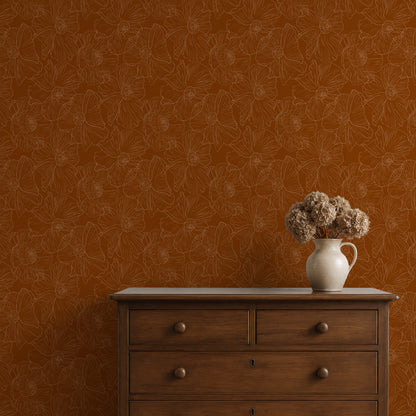 A styled interior scene showing a warm rust-orange wallpaper with a subtle floral line pattern, a dark wood dresser, and a white ceramic pitcher holding dried beige flowers.