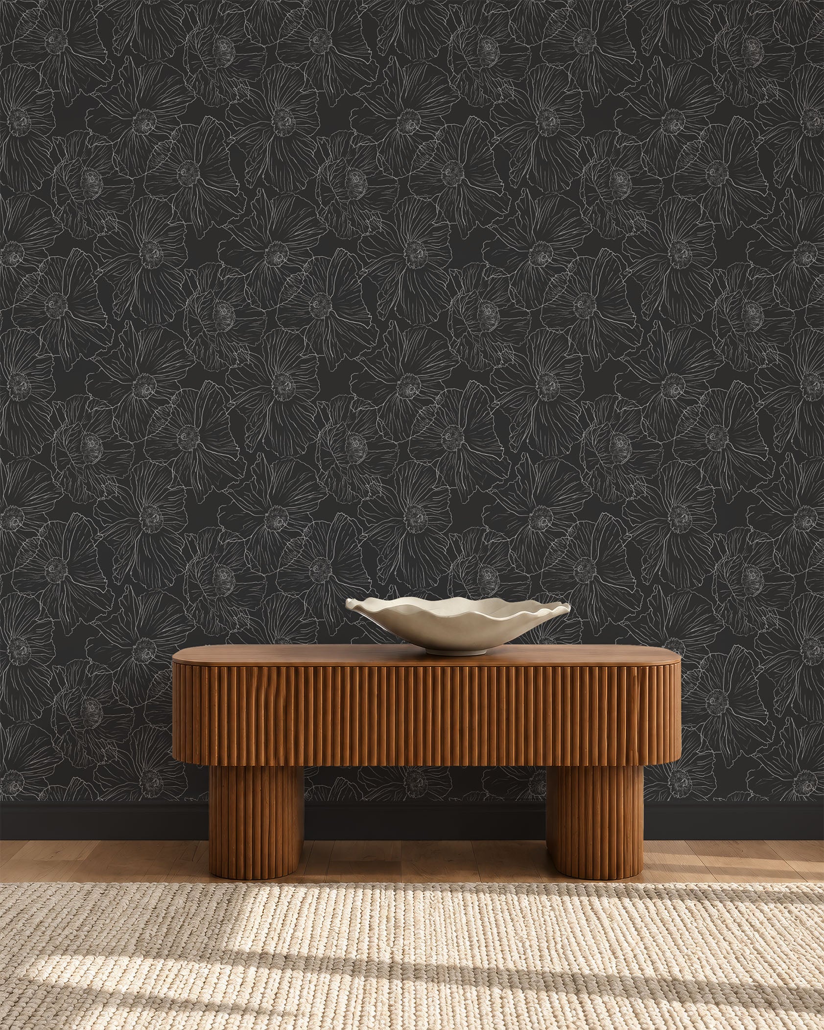 A styled interior scene showing a dark charcoal wallpaper with a fine light gray floral line pattern, a low ribbed wooden console table, a white ceramic bowl on top, and a woven rug on the floor.